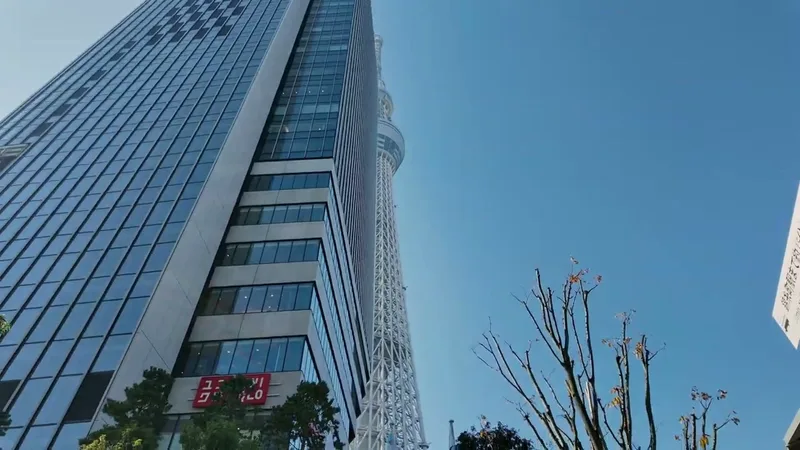 Low-angle view of Tokyo Skytree rising above the surrounding glass buildings against a clear blue sky in Tokyo, Japan