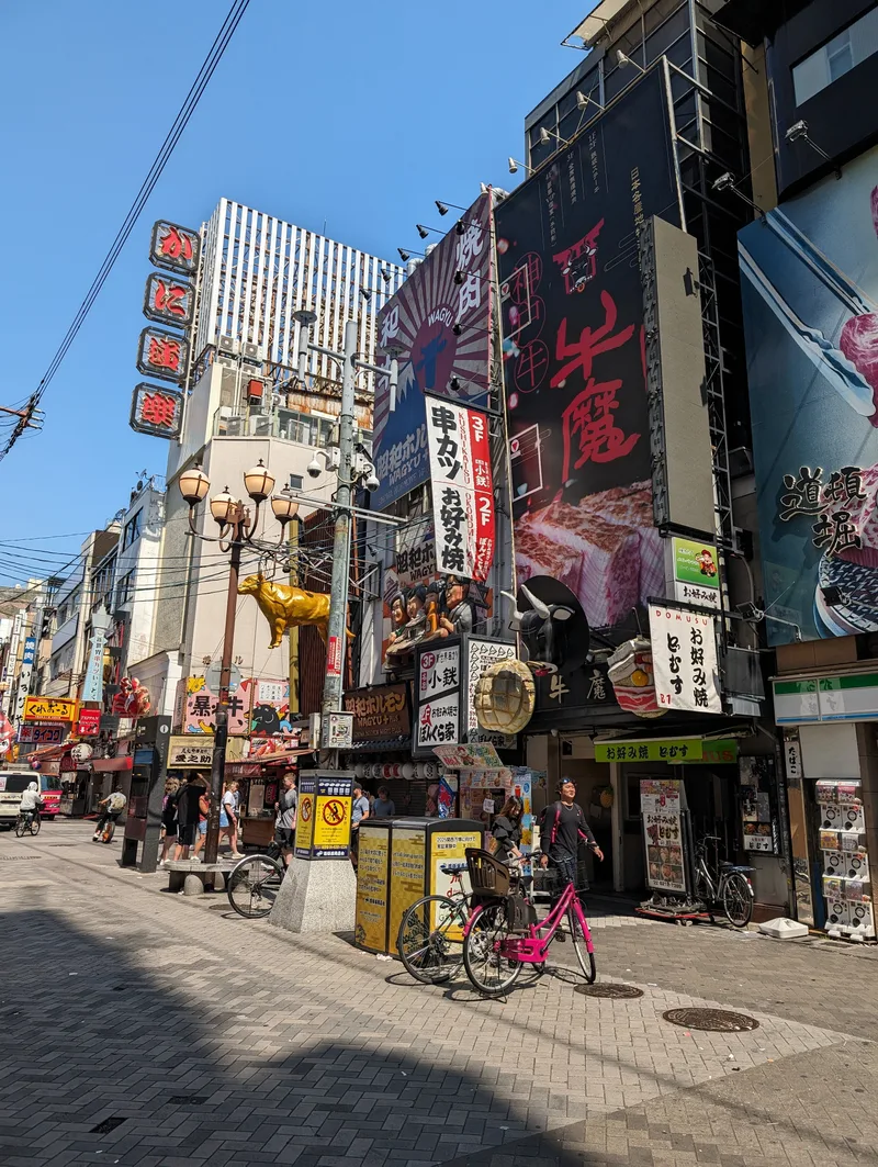 Busy street corner in Osaka, Japan, with colorful billboards, pedestrians, and a golden bull statue.