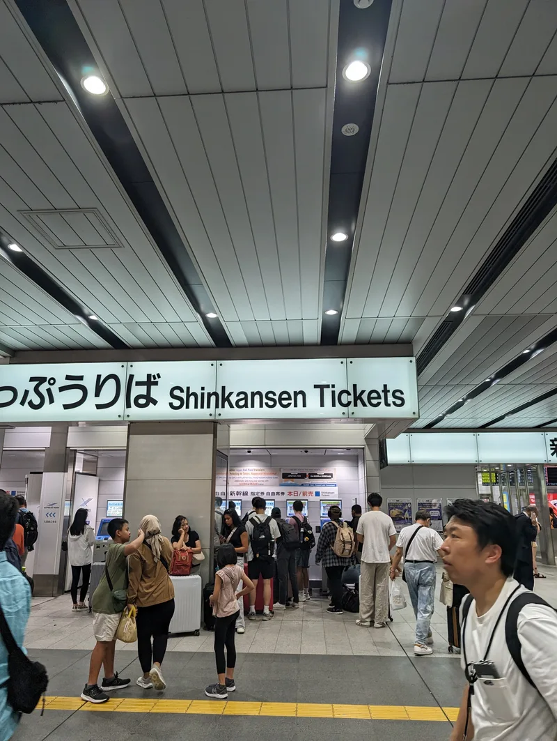 Busy Shinkansen ticket area in Shin-Osaka Station, Japan, with travelers at ticket machines and counters.