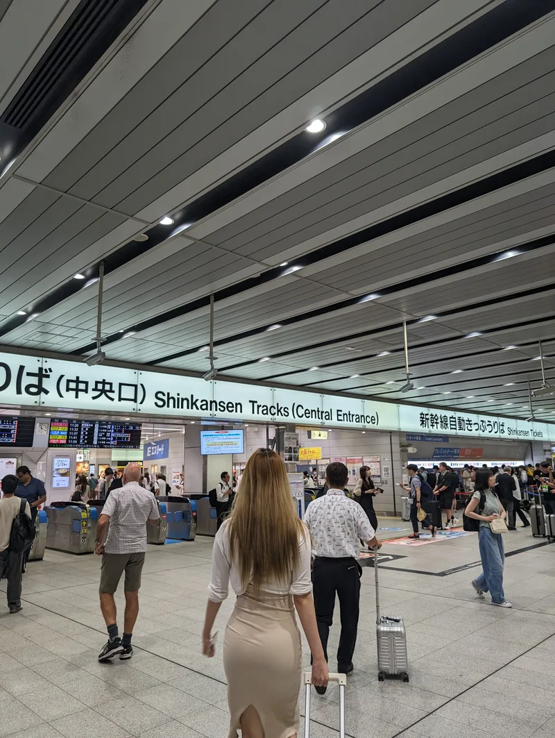 Wide Shinkansen tracks central entrance at Shin-Osaka Station, Japan, with travelers and luggage.