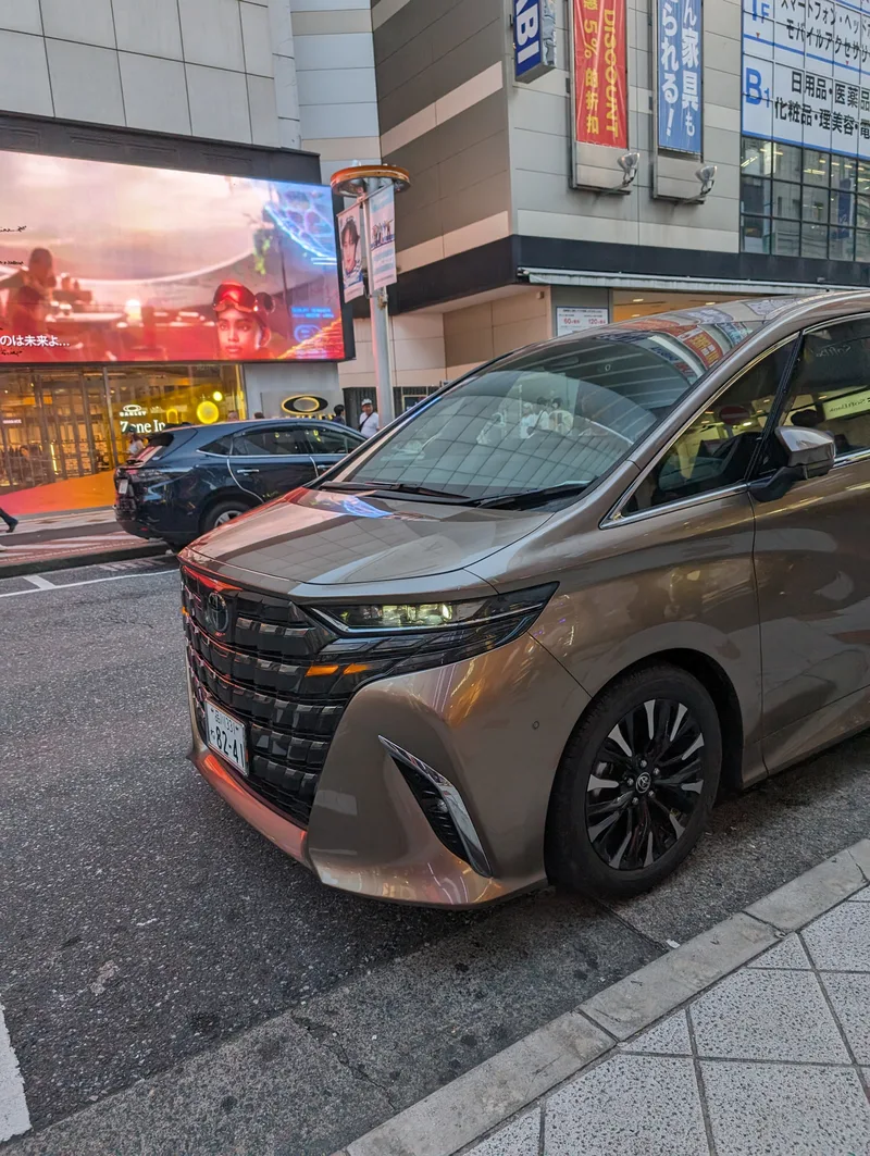 Front-side view of a gold Toyota Alphard minivan parked on a street in Shibuya, Tokyo, Japan.