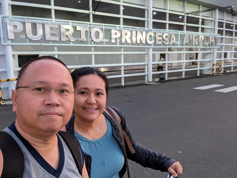 Couple selfie in front of the Puerto Princesa Airport sign on the terminal building exterior in Palawan