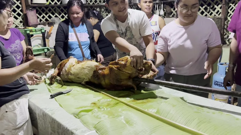 Filipino lechon roasted whole pig on a spit being carved surrounded by gathered family in Palawan