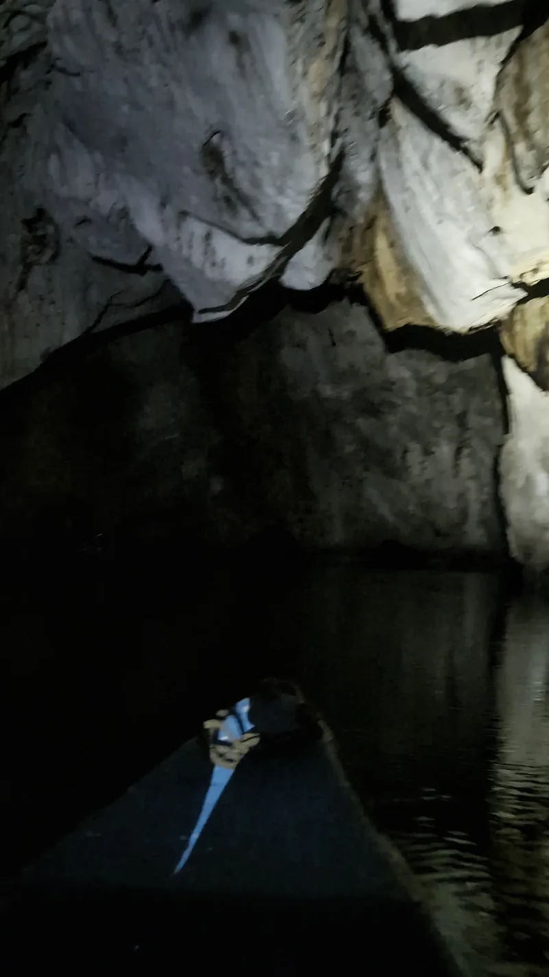 Dark atmospheric view from inside a boat on calm water within a cave with illuminated limestone rock formations on the ceiling and walls reflecting on the water at the Puerto Princesa Subterranean River, Palawan, Philippines