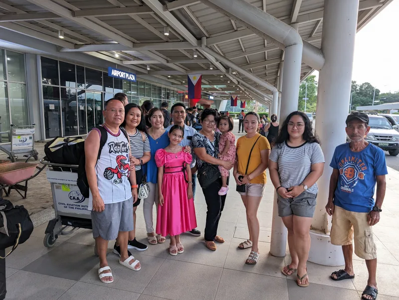 Large family group posing for a photo outside the Puerto Princesa airport terminal with the Philippine flag visible in the background Palawan Philippines