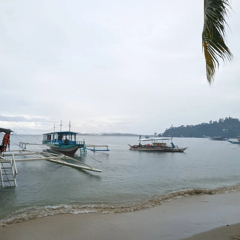 Two traditional Filipino bangka outrigger boats anchored in calm grey water on an overcast morning at the Sabang pier in Palawan Philippines