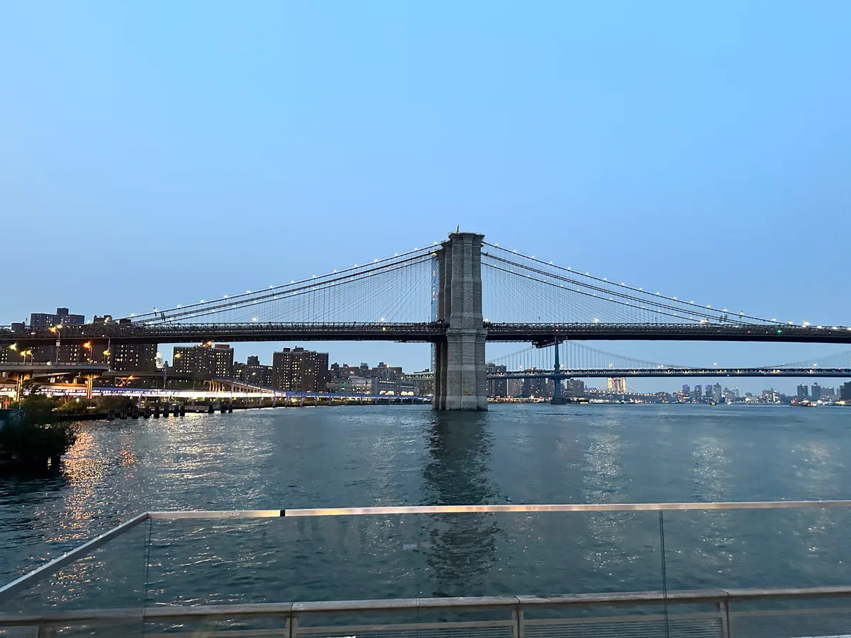 Brooklyn Bridge and Manhattan Bridge over East River with illuminated NYC skyline at dusk
