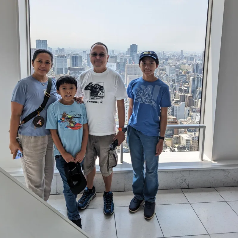 Family at Umeda Sky Building observation deck window with panoramic Osaka city view, Japan.