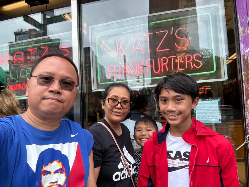 Family selfie in front of Katz's Delicatessen neon sign