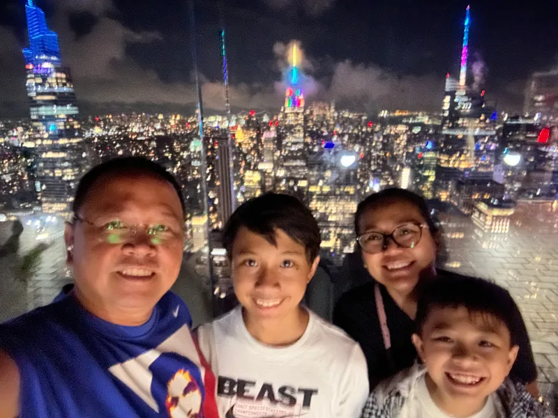Family selfie at Top of the Rock with illuminated NYC skyline at night