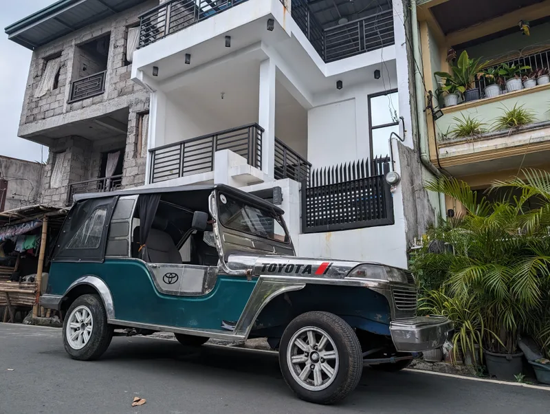Teal and silver Owner Type Jeep on a street in Liliw, Laguna, Philippines viewed from the front-side showing the hood and windshield.