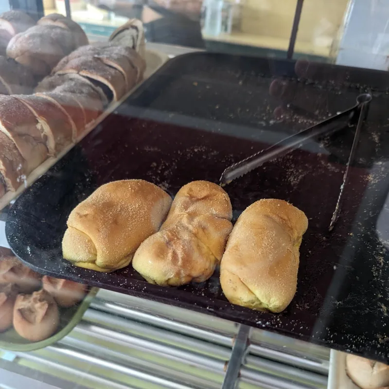 Three golden-brown sugar-dusted bread rolls on a black tray inside a bakery display case in Roxas Palawan Philippines
