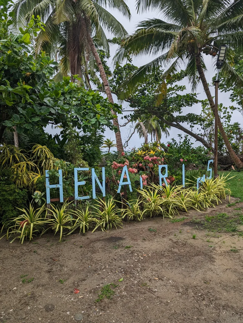 Large light blue HENARIS sign surrounded by tropical palm trees and plants at the beach resort in Caramay, Roxas, Palawan