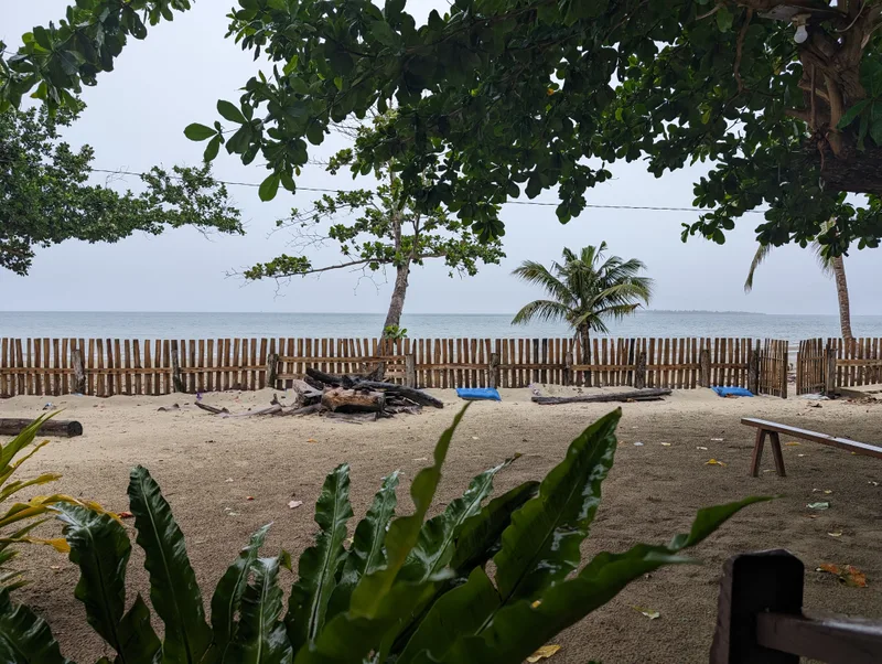 Wide view of sandy beach wooden fence and calm ocean with distant islands visible under an overcast sky at Henalric resort in Caramay Roxas Palawan