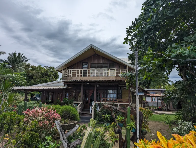 Two-story wooden house with balcony surrounded by lush tropical garden with cacti and flowering plants at Henalric resort in Palawan Philippines