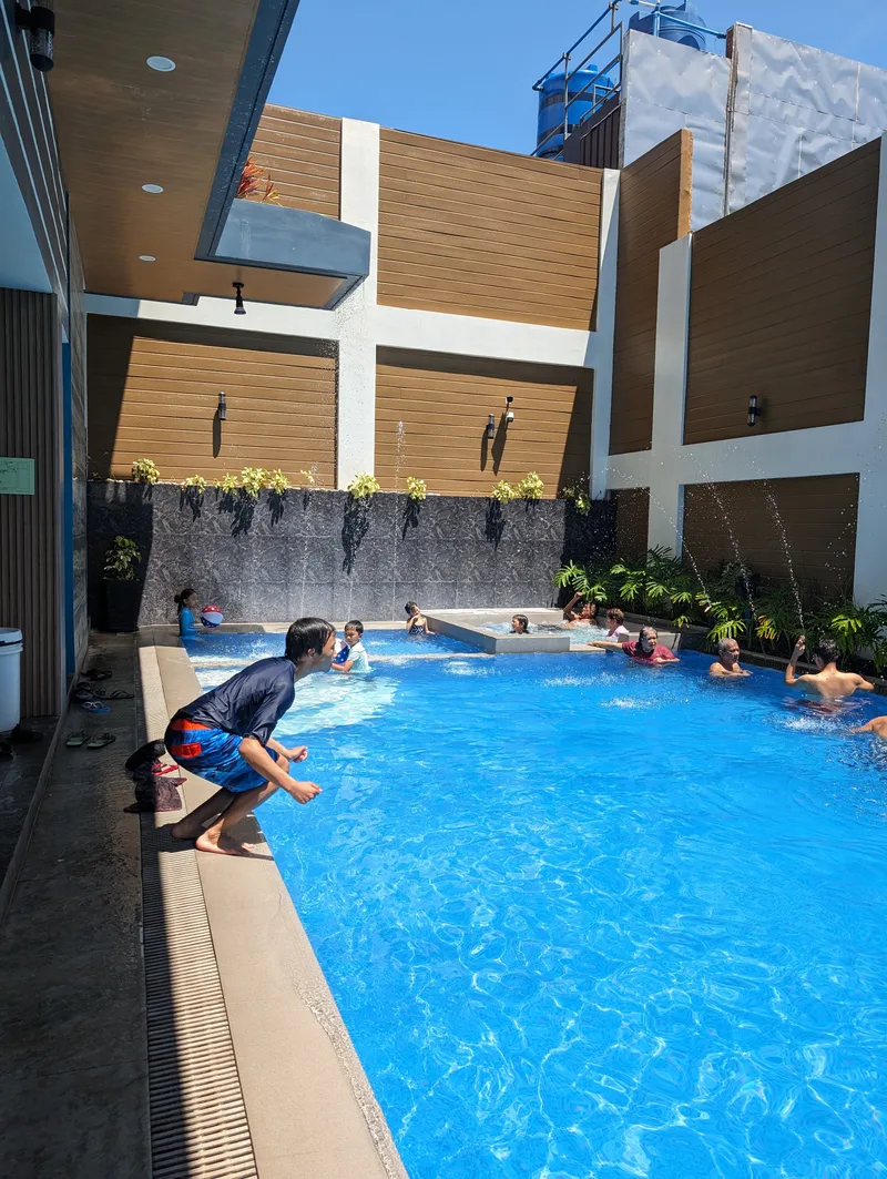 Young boy in blue shirt mid-jump into the sunny pool at Avery Ridge Resort, Pansol, Laguna, with other swimmers in the background.