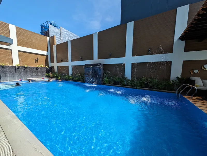 Sunny hotel swimming pool at Avery Ridge Resort in Pansol, Calamba with people swimming, waterfall, and modern architecture.