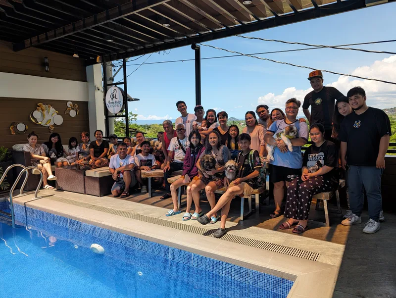 Large family group posing by the pool at Avery Ridge Resort in Pansol, Calamba, Laguna with dogs, children, and a panoramic view of green hills.